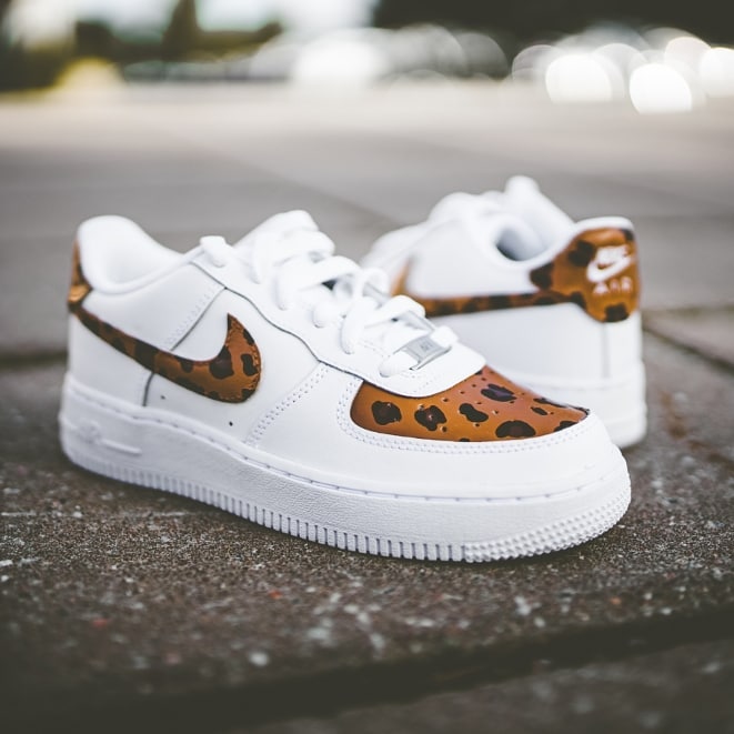 The image is featuring a custom hand painted cheetah print on a street background. The air force 1 shoes have a cheetah print design on the side and the front of shoes. 