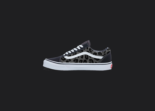 The image is featuring a custom hand painted cheetah print vans shoes on a blank black background. The vans old skools sneaker has a gray cheetah print design on the side of shoes.