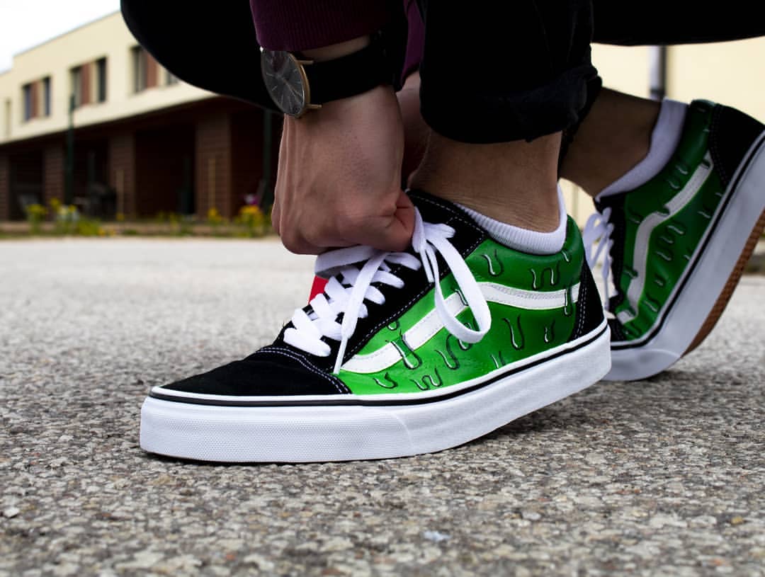 The image is featuring a custom hand painted green dripping shoes on a street background. The vand shoes have a dripping design on the side of shoes. 
