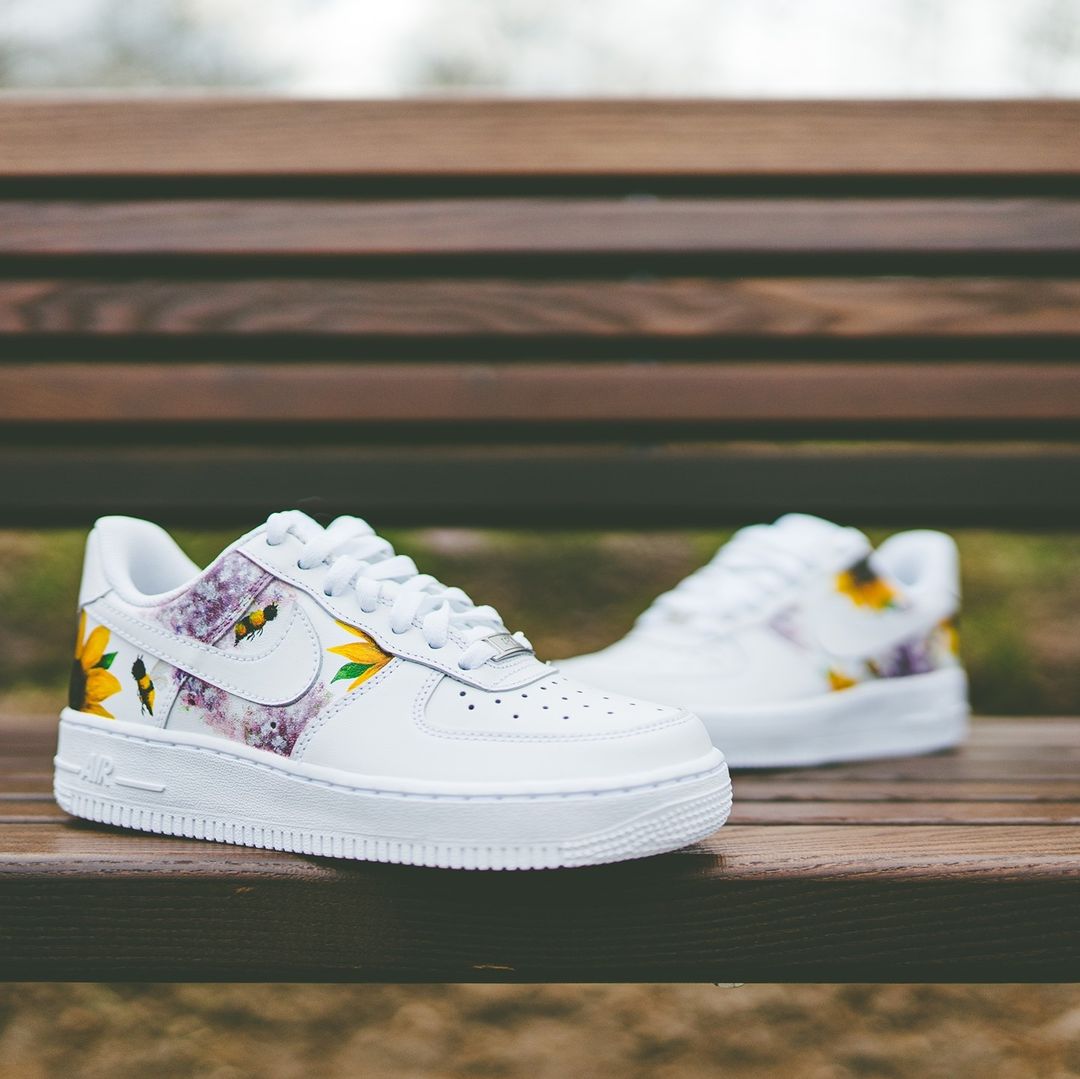 The image is featuring a custom hand painted floral shoes on a park bench background. The air force 1 sneaker has a floral print design on the side of shoes. 