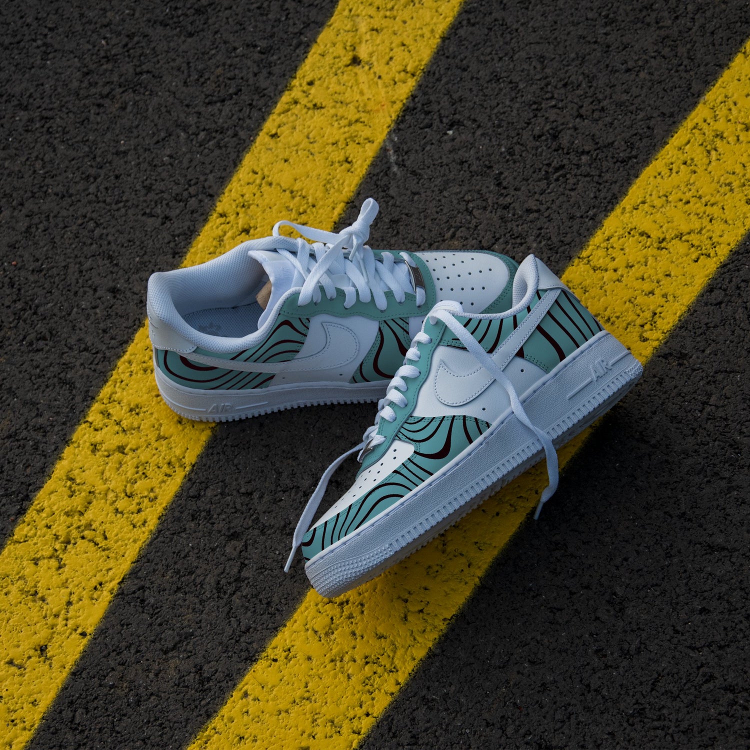 The image is of a Custom Nike Air force 1 sneaker on a street background. The white custom nike sneaker have a green and black design all over the sneakers.  