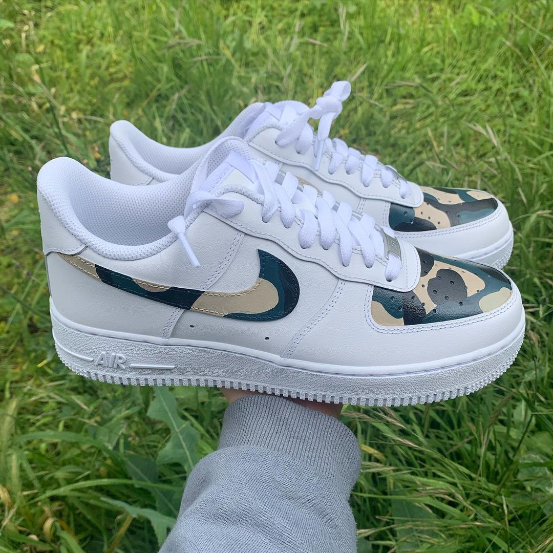 pair of nike air force 1s with a camo design on the nike swoosh and fron toe panel, grass background