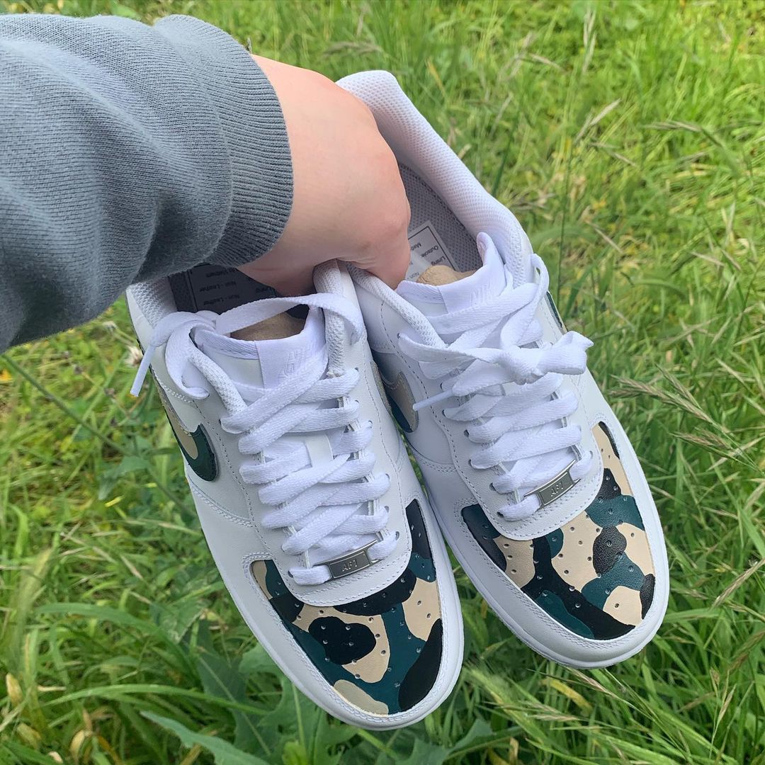 pair of nike air force 1s with a camo design on the nike swoosh and front toe panel, grass background