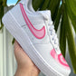 Custom Nike sneaker featuring a pink Swoosh and layered pink heart design on the front, set against a tropical background.