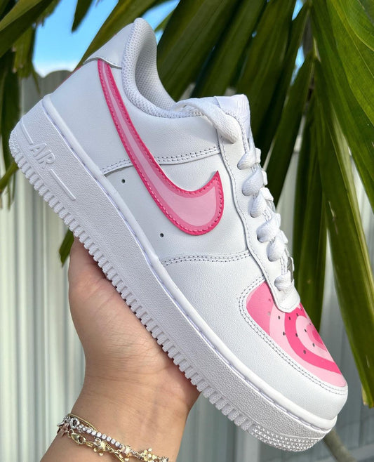 Custom Nike sneaker featuring a pink Swoosh and layered pink heart design on the front, set against a tropical background.