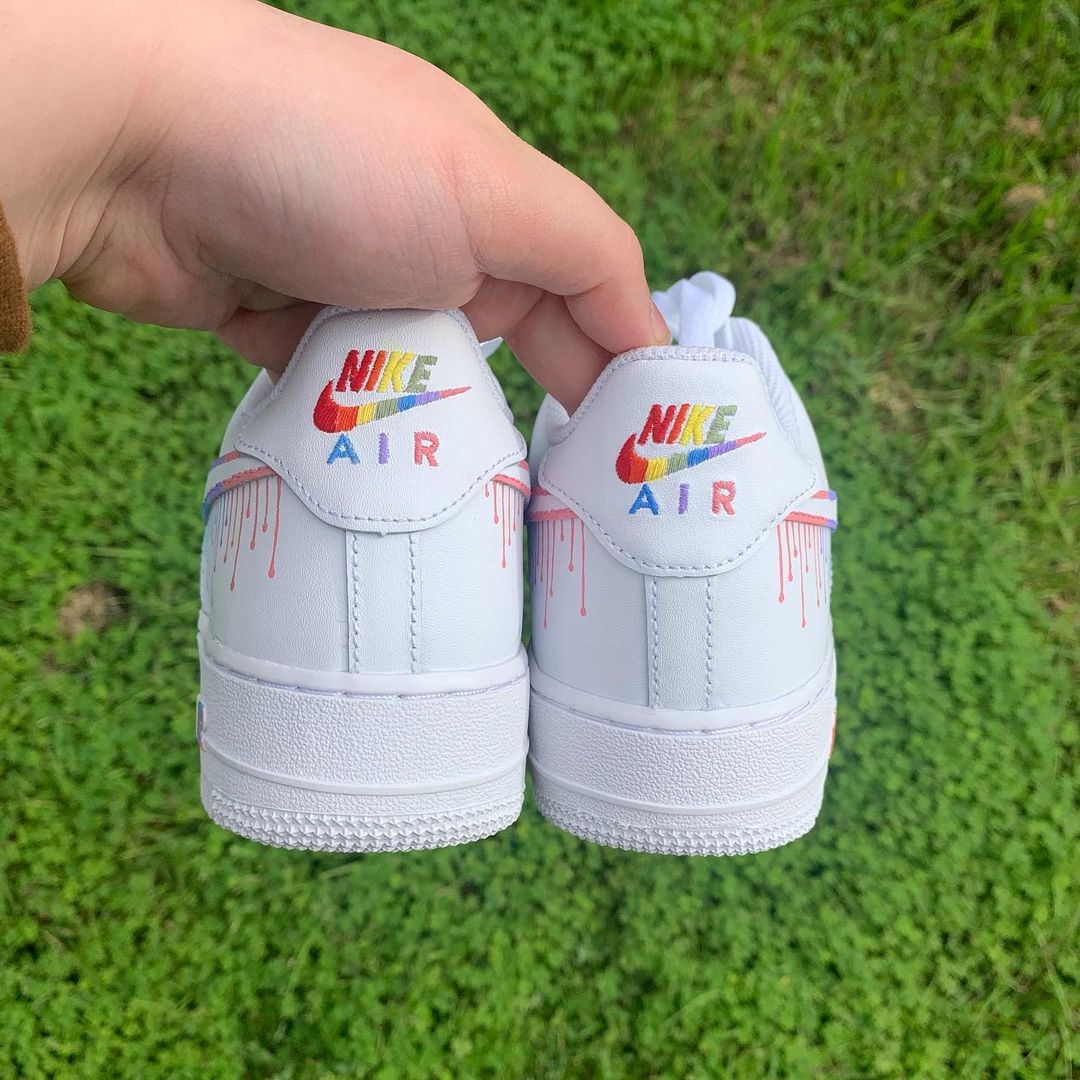 heel view pair of nike air force 1s with a colorful dripping design on the nike letters on the heel tab and on tthe side nike logos. Grass background