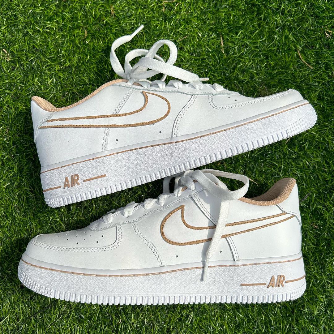 pair of nike air force 1s with a beige swoosh outline on the nike swoosh and beige colored insides of the white nike air force sneakers on a grass background