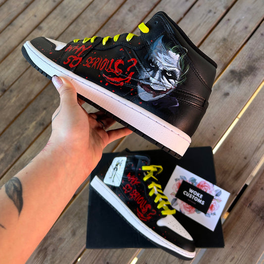 Pair of jordan 1 mid models with a cusotm hand painted design of joker on the side of the sneakers. In red you also have the text "why so serious" with some splatter covering the sides. With a terrace background