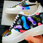 Side view of custom Nike sneakers with a lively camo pattern in multiple colors, featuring bright blue, pink, green, and purple shades on a black background.