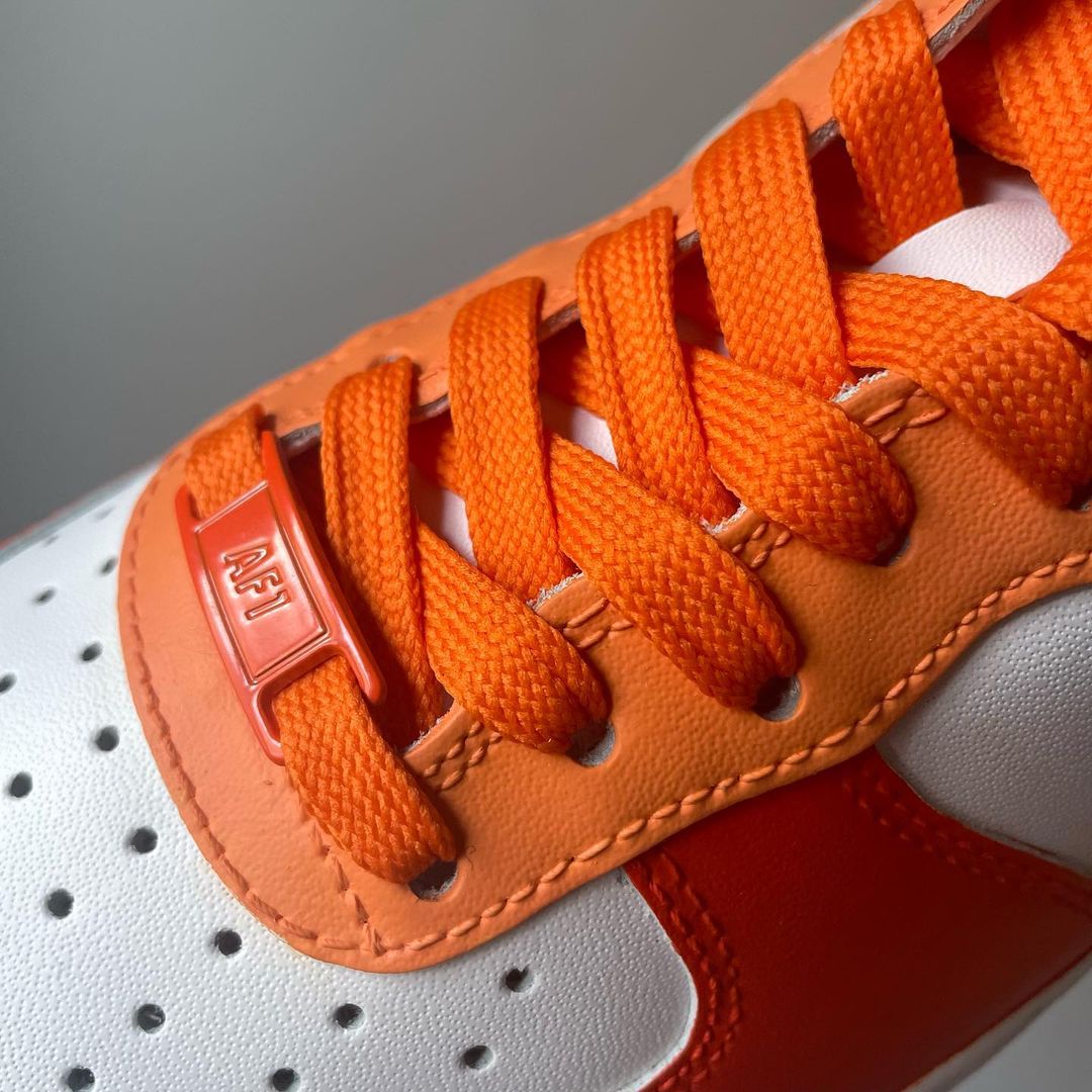 a closeup of a pair of nike air force 1s with a orange tones design on the outside sections of the sneakers. Orange laces and shoe tag Blank gray shadow wall on the background