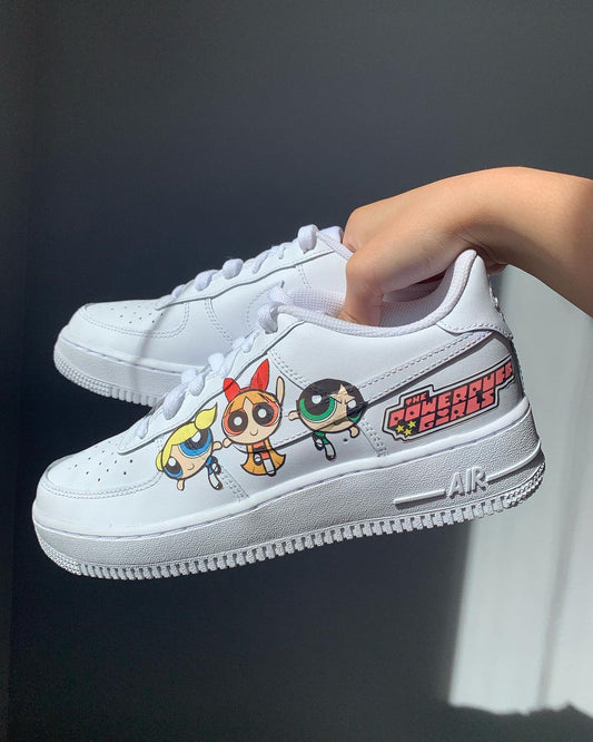 a pair of nike air force 1s with a powerpuff girls design on the outside sections of the sneakers. Blank gray shadow wall on the background