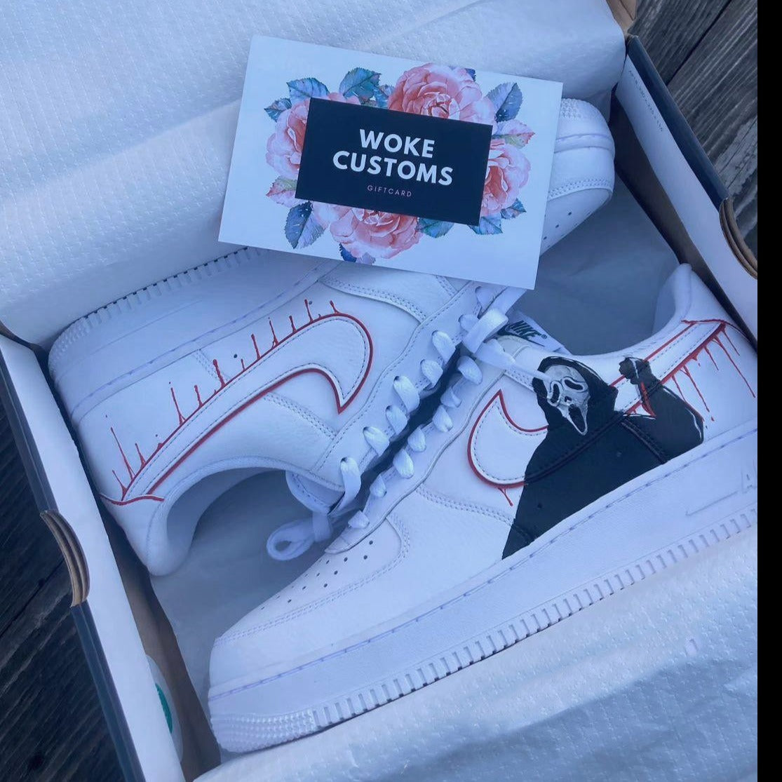 A pair of white sneakers with custom hand-painted designs featuring a ghostly figure and a dripping blood effect on the swoosh. The shoes are in a shoebox with a “Woke Customs” gift card.