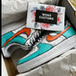 A pair of custom Nike Air Force 1 sneakers featuring a hand-painted design with vibrant turquoise and orange accents. The shoes are displayed in an open box, with a “WOKE CUSTOMS” gift card placed on top. The gift card has a floral border and a black rectangle with white text.