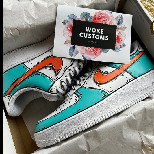 A pair of custom Nike Air Force 1 sneakers featuring a hand-painted design with vibrant turquoise and orange accents. The shoes are displayed in an open box, with a “WOKE CUSTOMS” gift card placed on top. The gift card has a floral border and a black rectangle with white text.
