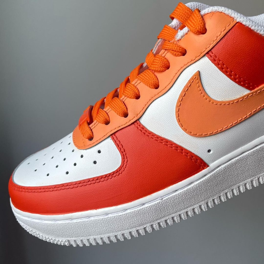 a single sneaker of nike air force 1 with orange tones design on the outside sections of the sneakers. Orange laces. Blank gray shadow wall on the background