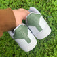 Back view pair of nike air force 1s with a pastel green design on the heel tab, grass background