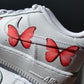 a closup of a nike air force 1 sneaker with a simple red butterfly design on the outside sections of the sneakers. Blank gray shadow wall on the background