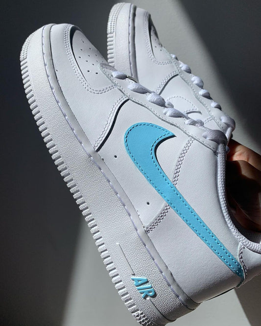 a pair of nike air force 1s with a simple blue handpainted nike logo and sole design on the side of the sneakers. Blank gray shadow wall on the background