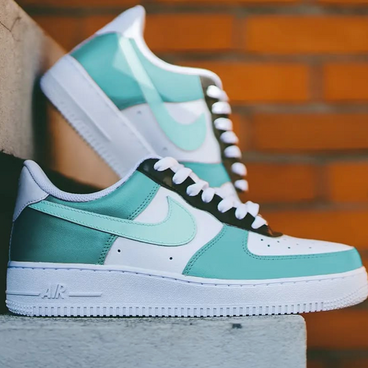 a pair of custom white nike air force 1s painted in light baby blue tones and a darker black sneaker laces section. the pair is placed on a rock staircase
