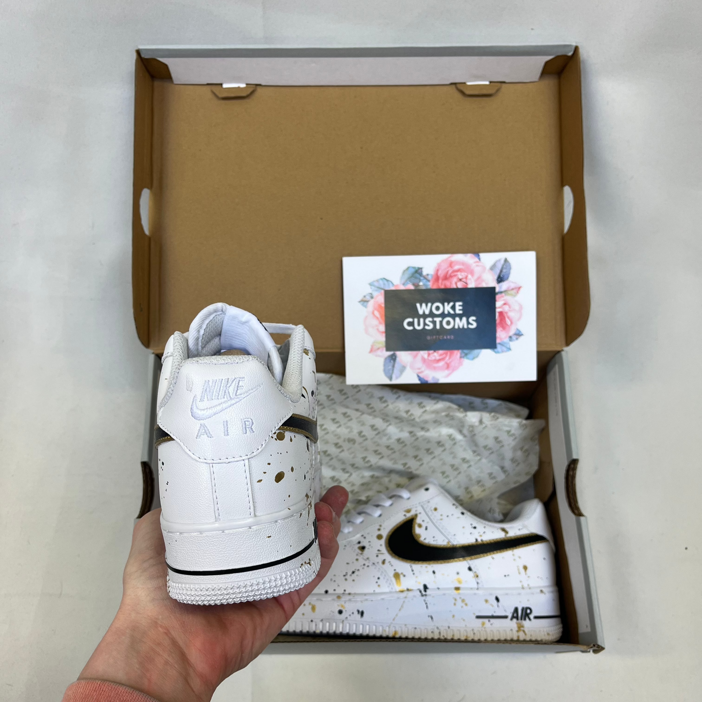Custom white Nike Air Force 1 with gold and black paint splatter design, handpainted custom sneakers showing heel view with Nike Air branding