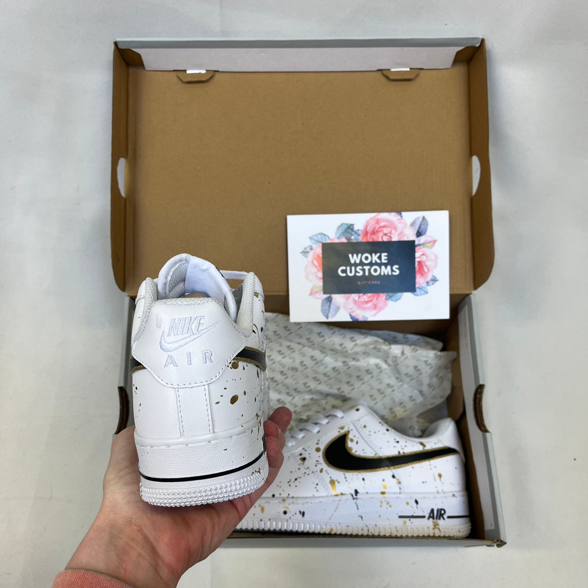 Custom white Nike Air Force 1 with gold and black paint splatter design, handpainted custom sneakers showing heel view with Nike Air branding