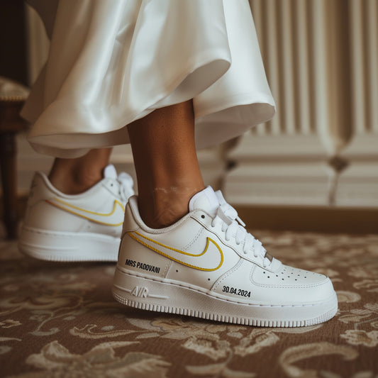 woman in white dress wearing white nike air force 1 sneakers with gold outline swoosh and name and date printed on the outside of the sneaker in black