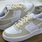 pair of nike air force 1s with a light beige design on the sections of the sneakers. Sneakers have a the same light colored beige painted laces. Sneakers have a white sole