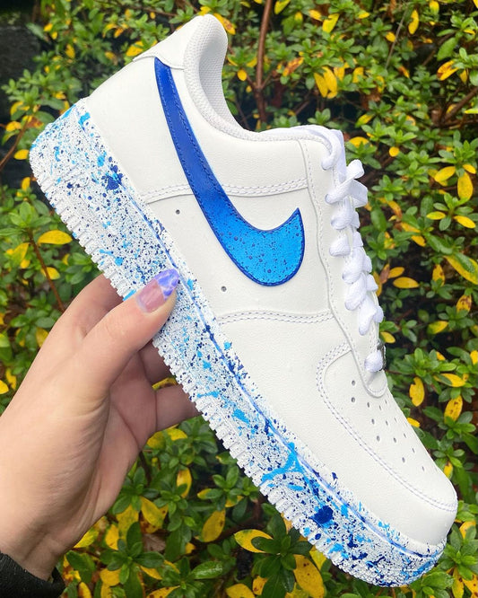 Close-up of a custom Nike Air Force 1 sneaker featuring a bold blue swoosh with a splatter fade effect. The blue gradually transitions into a white midsole, creating a striking, hand-painted design with vibrant blue accents.