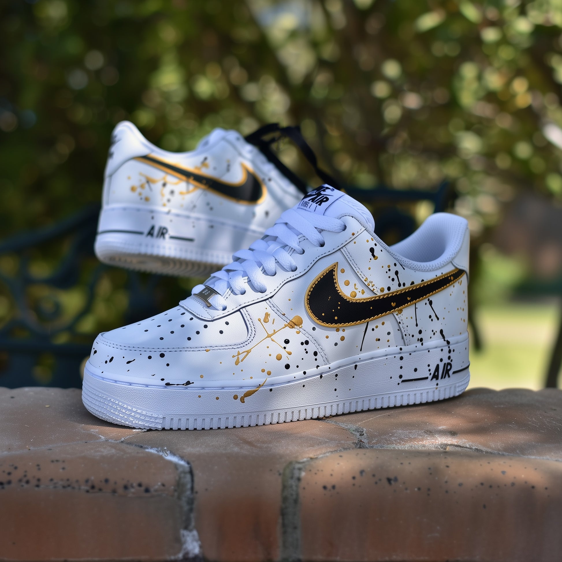white nike air force 1s with a gold and black splatter desing on all sides of the sneakers. nike logo is painted in black with a gold outline. Paint splatter in gold and black covering the sides of the sneakers