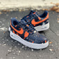 white nike air force 1s covered in navy blue with orange nike logos and orange paint splatter all over the sneakers. Sneakers have  a white sole and navy blue shoelaces. Design is on all sides. 