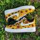white nike air force 1s with a handpainted sunflower print design covering bot sides of the sneakers. sneakers have a white sole and laces. picture is taken on a grass background. 