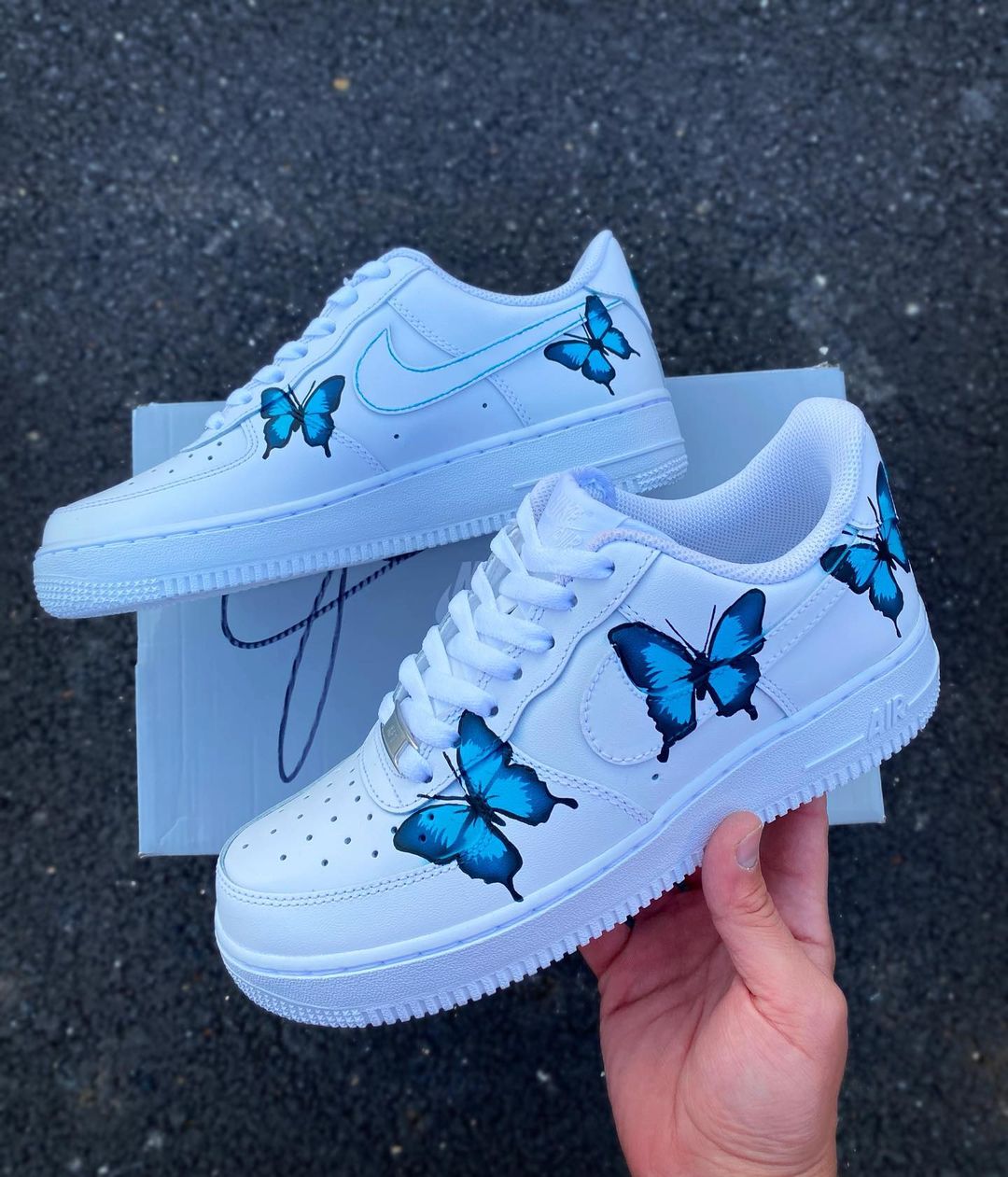 Pair of custom Nike Air Force 1 sneakers featuring handpainted blue butterflies in a natural, flowing design.