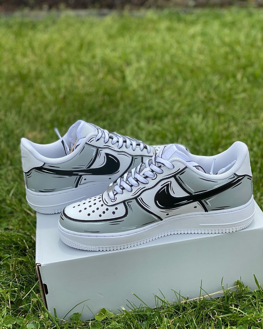 Pair of custom comic-inspired Nike Air Force 1 sneakers with bold black outlines and a cartoon effect, displayed on grass.