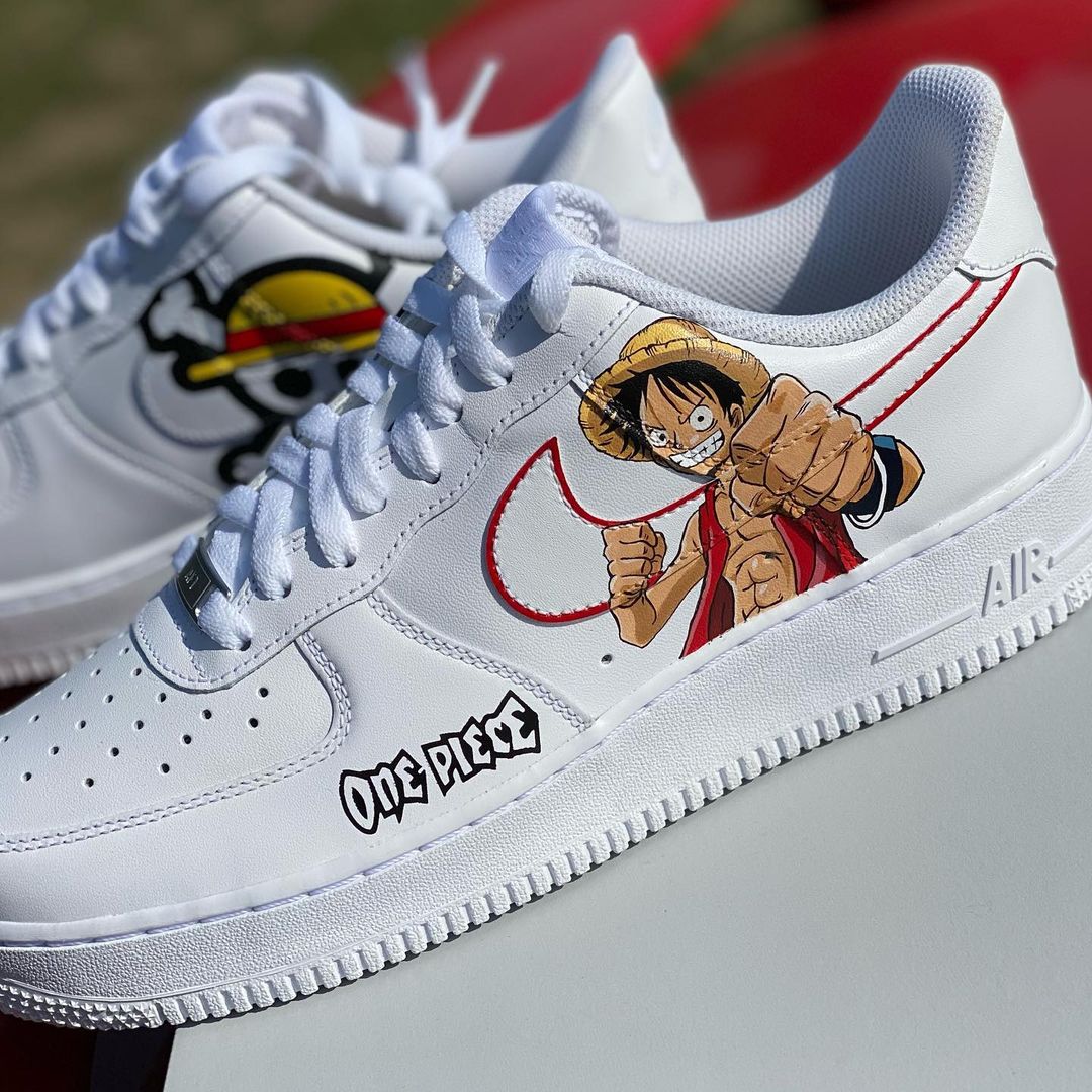 Pair of custom Nike Air Force 1 sneakers with “One Piece” anime character and logo, featuring a striking red swoosh and detailed artwork.