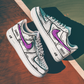 pair of white nike air force 1s with a cartoon design and a purple nike logo. background is a tenniscourt