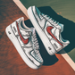 pair of white nike air force 1s with a cartoon design and a red nike logo. background is a tenniscourt
