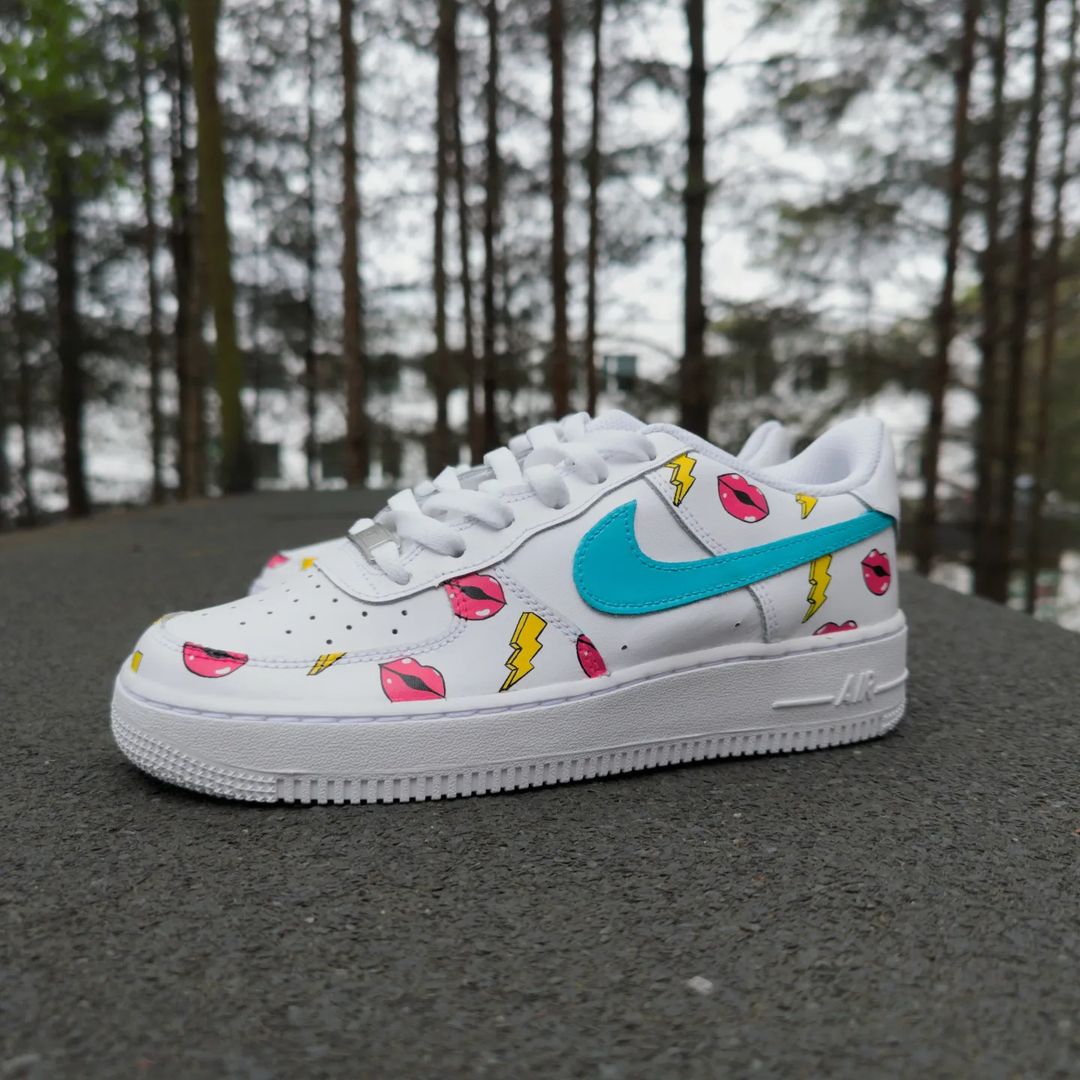 Custom Nike Air Force 1 sneakers with a pop art design featuring bright pink lips and yellow lightning bolts, complemented by a teal blue Nike swoosh. Hand-painted by Woke Customs for a bold, vibrant look.