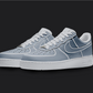 The image is featuring a Custom blue cartoon Air force 1 sneaker pair on a blank black background. The white nike sneakers have a blue cartoon design on the entire air force sneakers. 