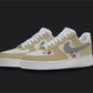 The image is of a Custom Nike Air force 1 sneaker pair on a blank black background. The white custom sneakers have a beige tone with floral illustrations on the sides.