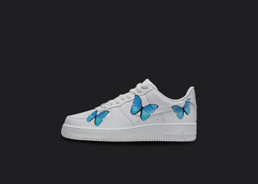 The image is of a Custom Nike Air force 1 sneaker on a blank black background. The white custom sneaker have a blue butterfly design on the sides. 