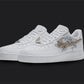 The image is of a Custom Nike Air force 1 sneaker pair on a blank black background. The white custom sneakers have a beige nike logo with floral illustrations on the sides.