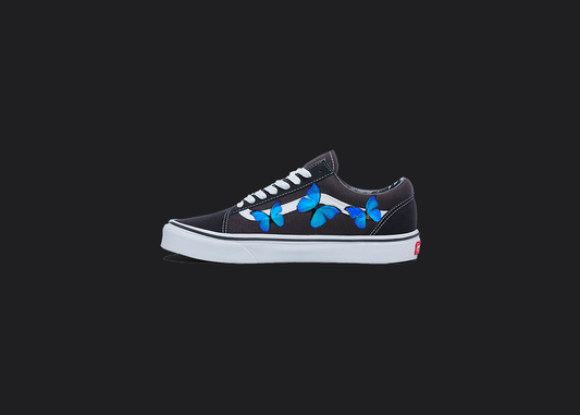 The image is featuring a custom hand painted vans shoes on a blank black background. The vans old skools sneaker has a custom blue Butterfly design on the side of shoes. 
