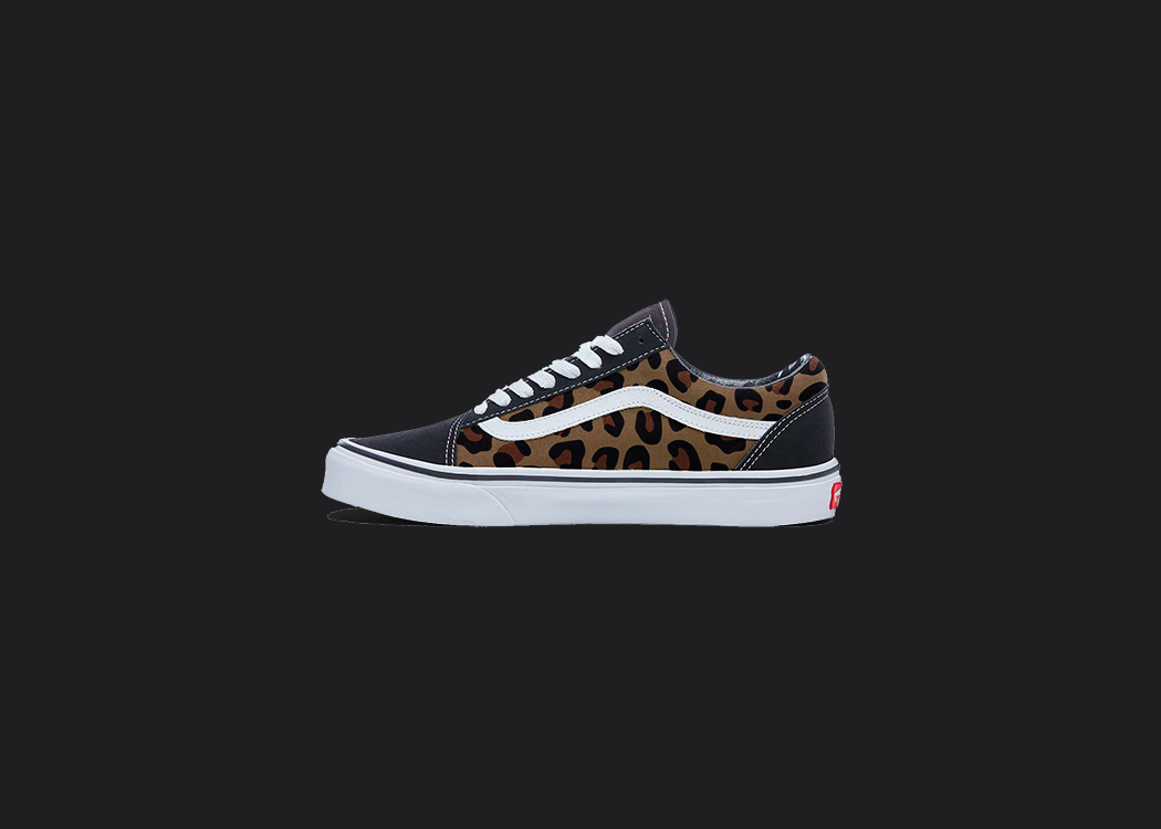 The image is featuring a custom hand painted cheetah print vans shoes on a blank black background. The vans old skools sneaker has a brown cheetah print design on the side of shoes.