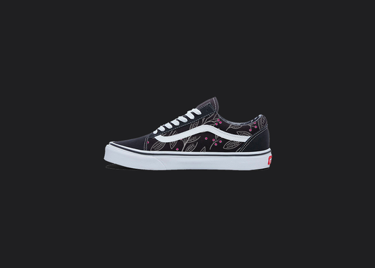 The image is featuring a custom hand painted floral shoes on a blank black background. The vans old skools sneaker has a pink floral print design on the side of shoes. 