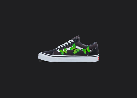 The image is featuring a custom hand painted vans shoes on a blank black background. The vans old skools sneaker has a custom green Butterfly design on the side of shoes. 