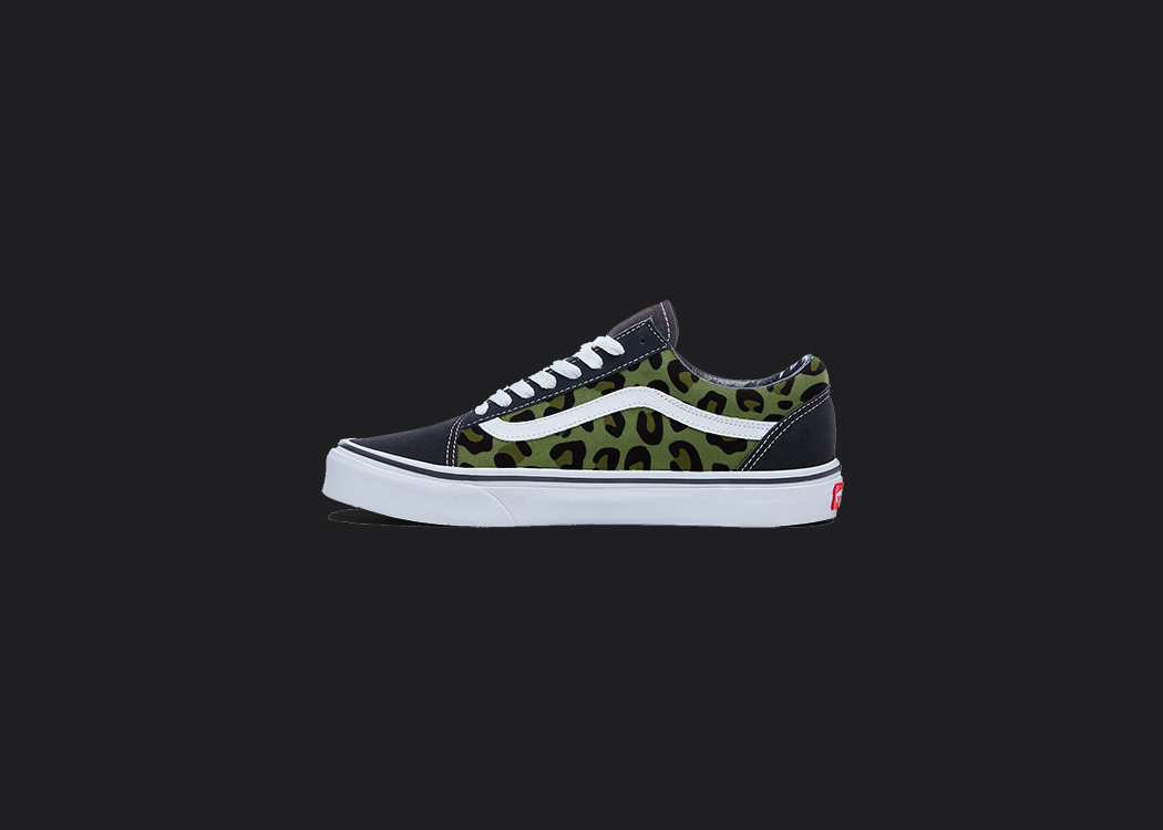 The image is featuring a custom hand painted cheetah print vans shoes on a blank black background. The vans old skools sneaker has a green cheetah print design on the side of shoes.
