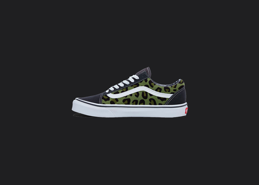 The image is featuring a custom hand painted cheetah print vans shoes on a blank black background. The vans old skools sneaker has a green cheetah print design on the side of shoes.
