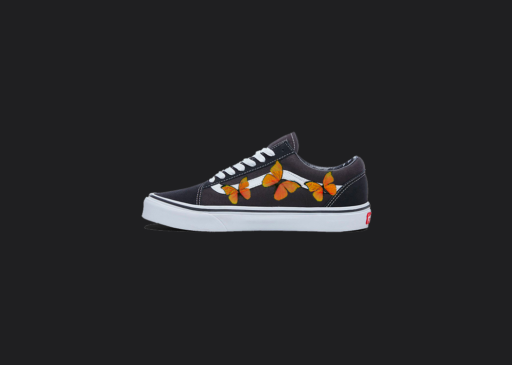 The image is featuring a custom hand painted vans shoes on a blank black background. The vans old skools sneaker has a custom orange Butterfly design on the side of shoes. 