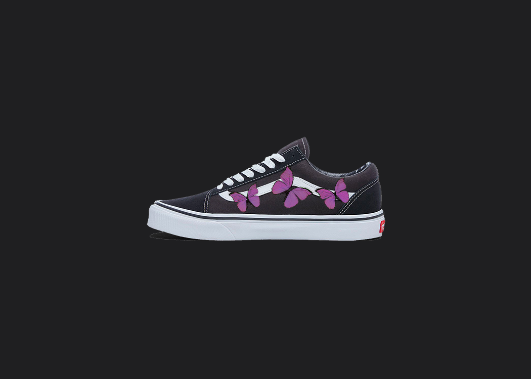 The image is featuring a custom hand painted vans shoes on a blank black background. The vans old skools sneaker has a custom pink Butterfly design on the side of shoes. 