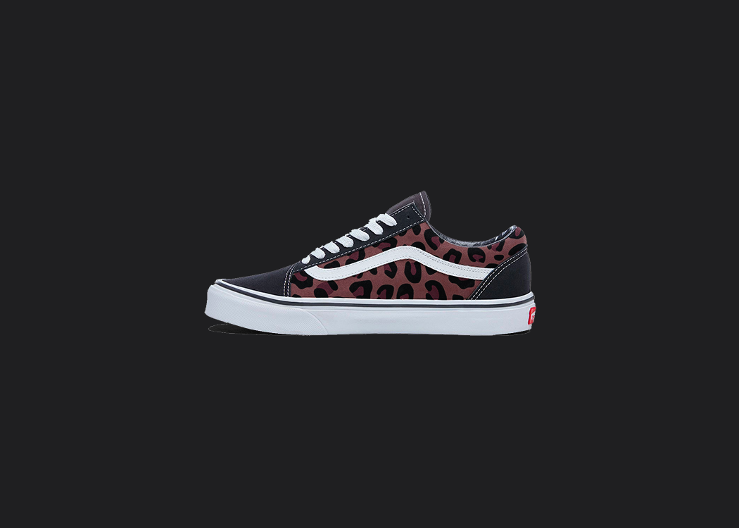 The image is featuring a custom hand painted cheetah print vans shoes on a blank black background. The vans old skools sneaker has a red cheetah print design on the side of shoes. 